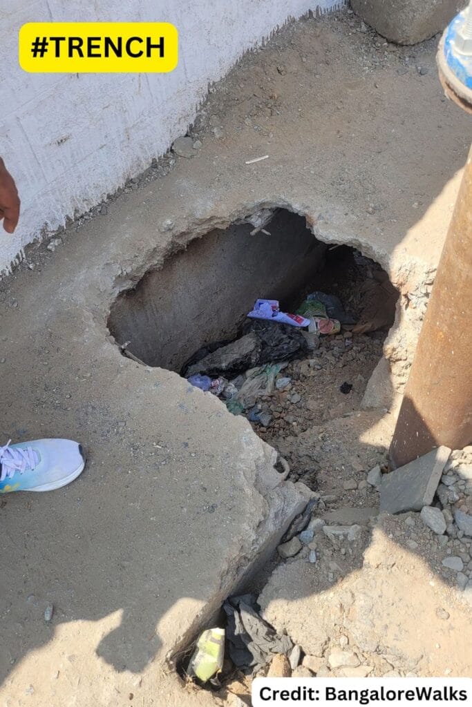 deep hole in the concrete footpath strewn with garbage