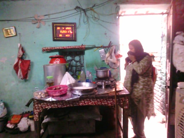 Woman cooking inside her room on a stove placed on a table.